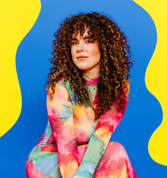 Claire Pongonis - Creative artist in bright dress in front of shape background - fiber and embroidery artist and creative at Kaleidoscope Collective in Northwest Arkansas