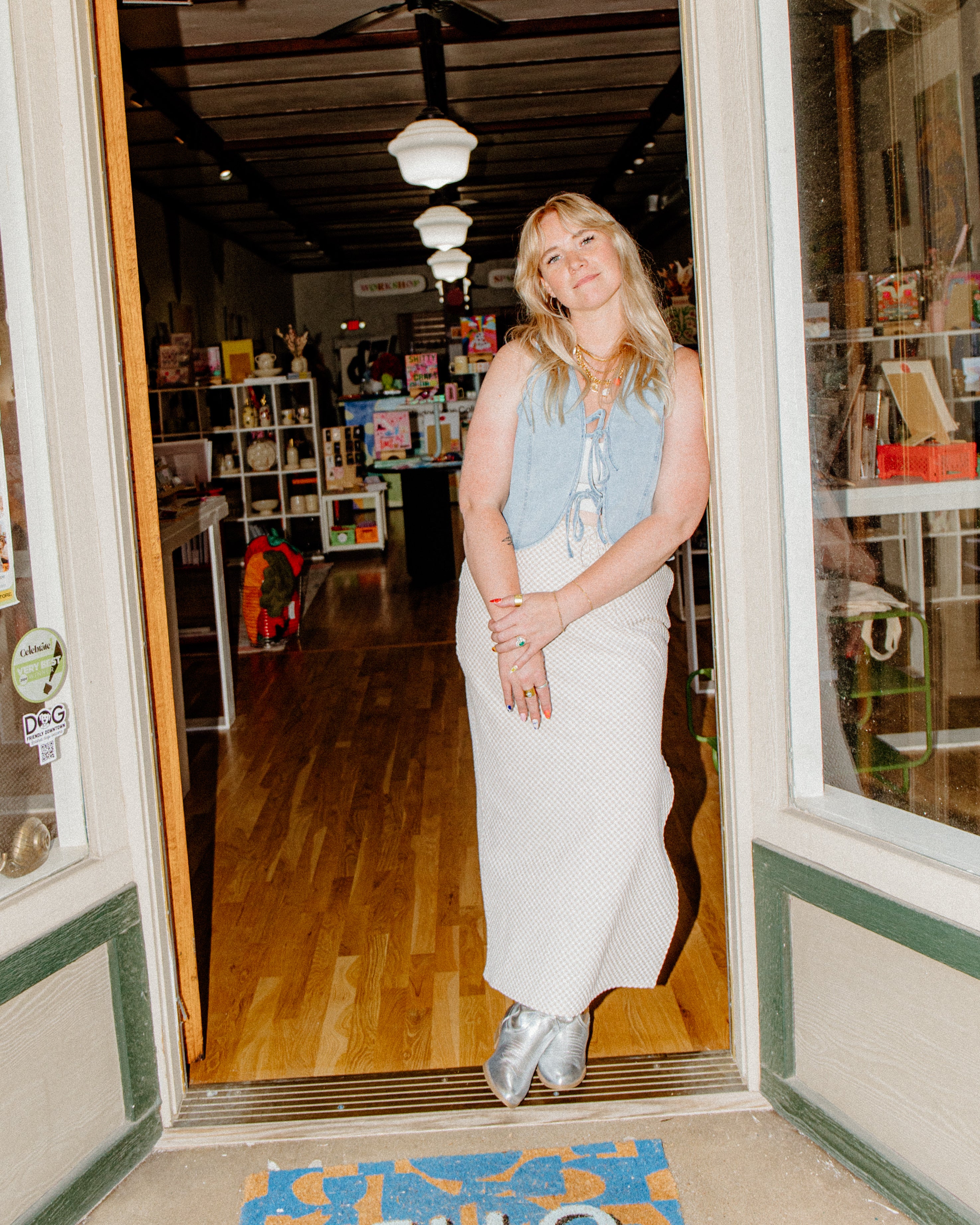White Blonde Women standing in doorwar of Arkansas Local Art Store Kaleidoscope Collective curator owner Kaleidoscope Collective in Rogers Arkansas Downtown Art Shop 